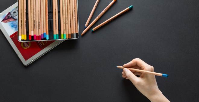 A hand holding one colored pencil from a nearby set